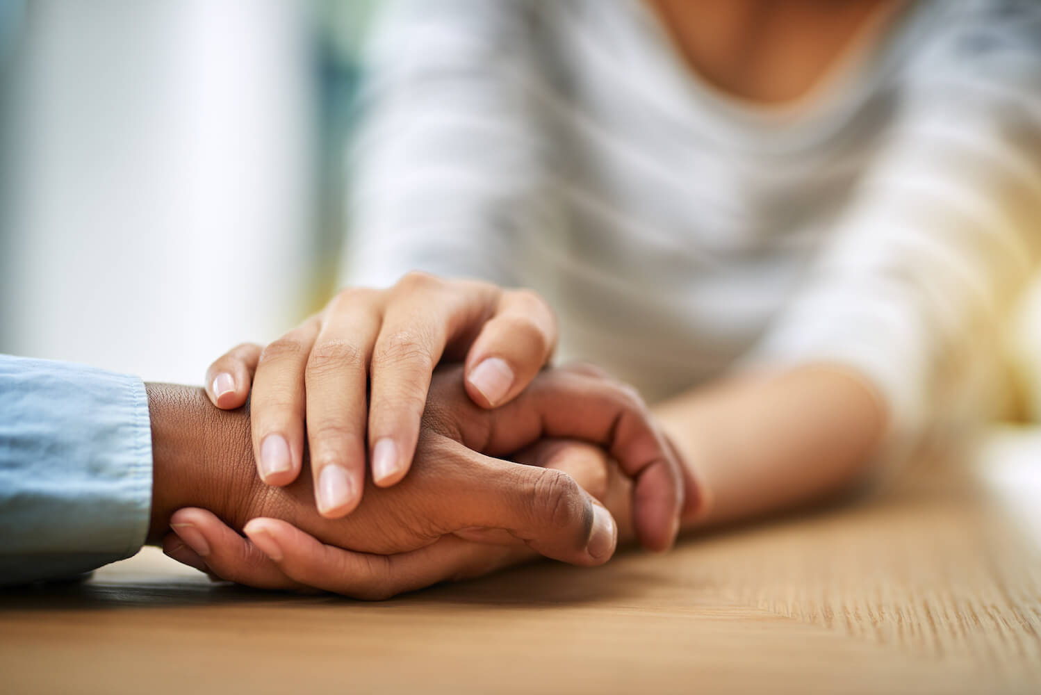 Cropped shot of two people holding hands while being seated at a table inside 